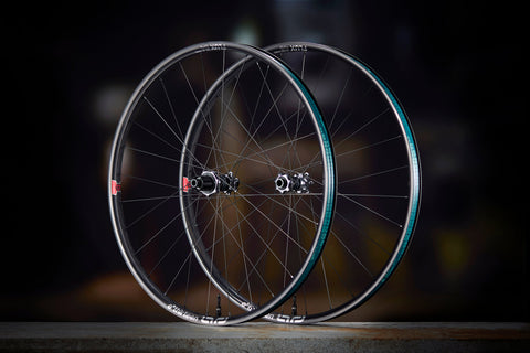 A Sidekick Flux front and rear wheel standing side by side on a dark floor, Flux rims with the teal rim-bed decal and Sidekick hubs.