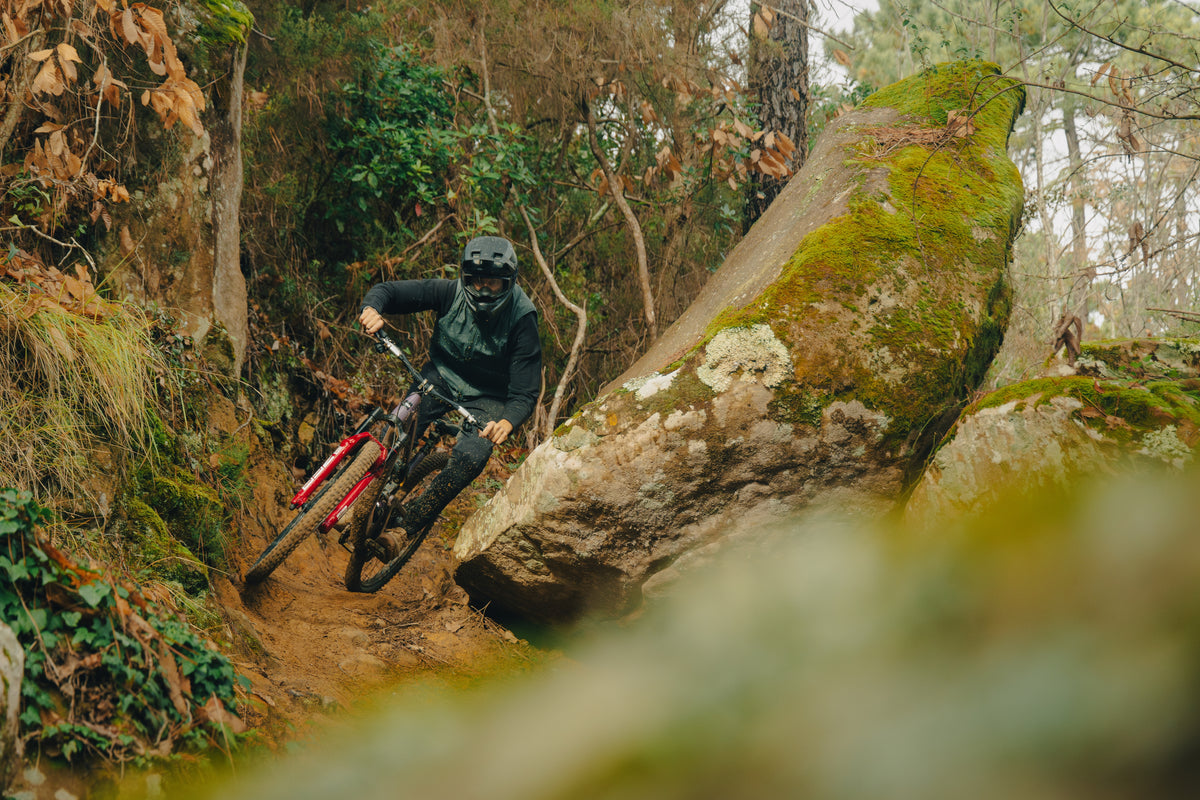 Rider threading a rocky chute between mossy boulders on an enduro trail.
