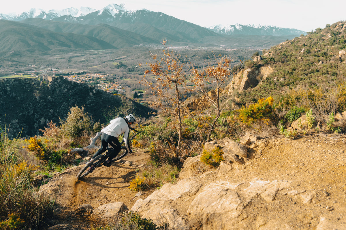 Rider carving a dusty trail corner above a valley, snow-capped mountains behind.