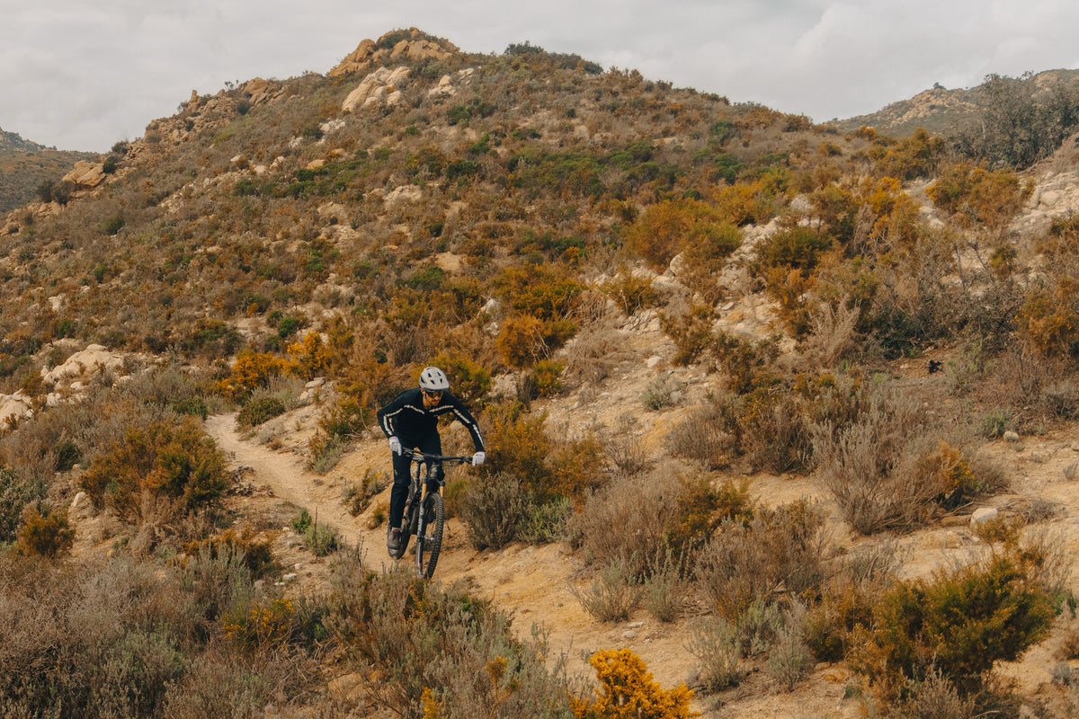 Rider on Sidekick Flux wheels climbing a dry singletrack through scrub, cross-country terrain.