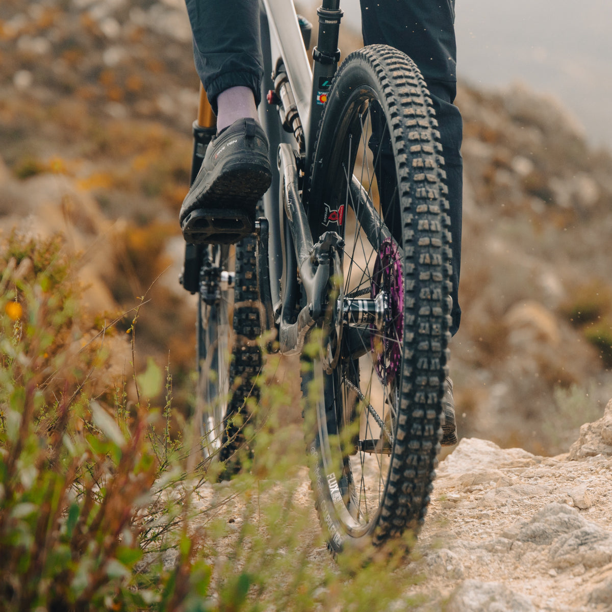 A Grappler TR front tire and a rider's foot on the pedal, on a dry hillside trail.