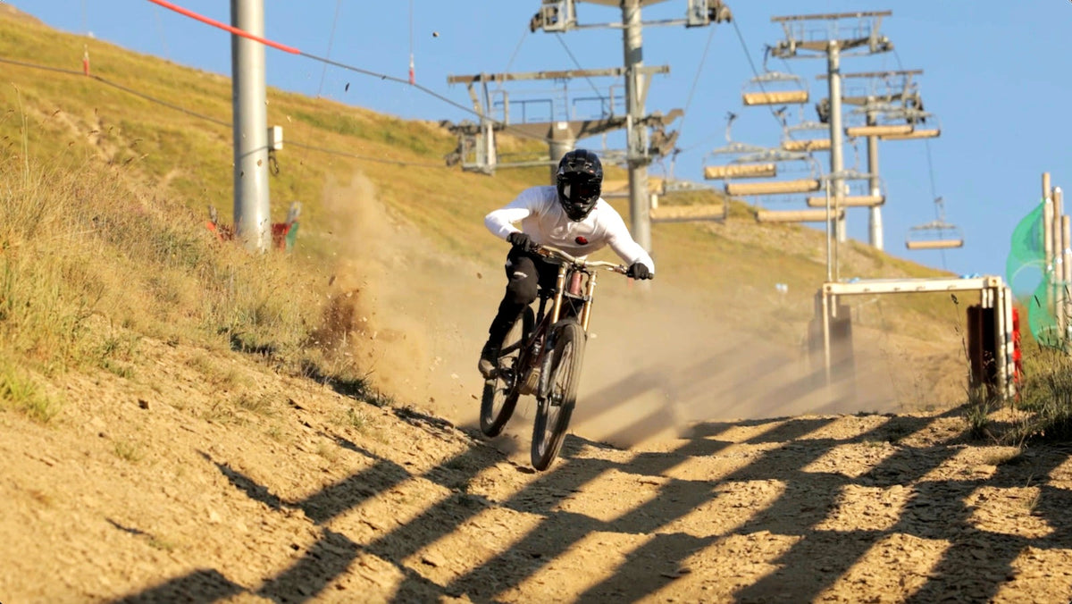 A rider drifting a dusty bike park turn under a chairlift