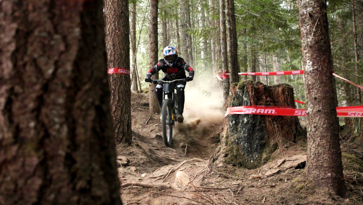 A downhill racer on course between trees, SRAM tape strung along the track